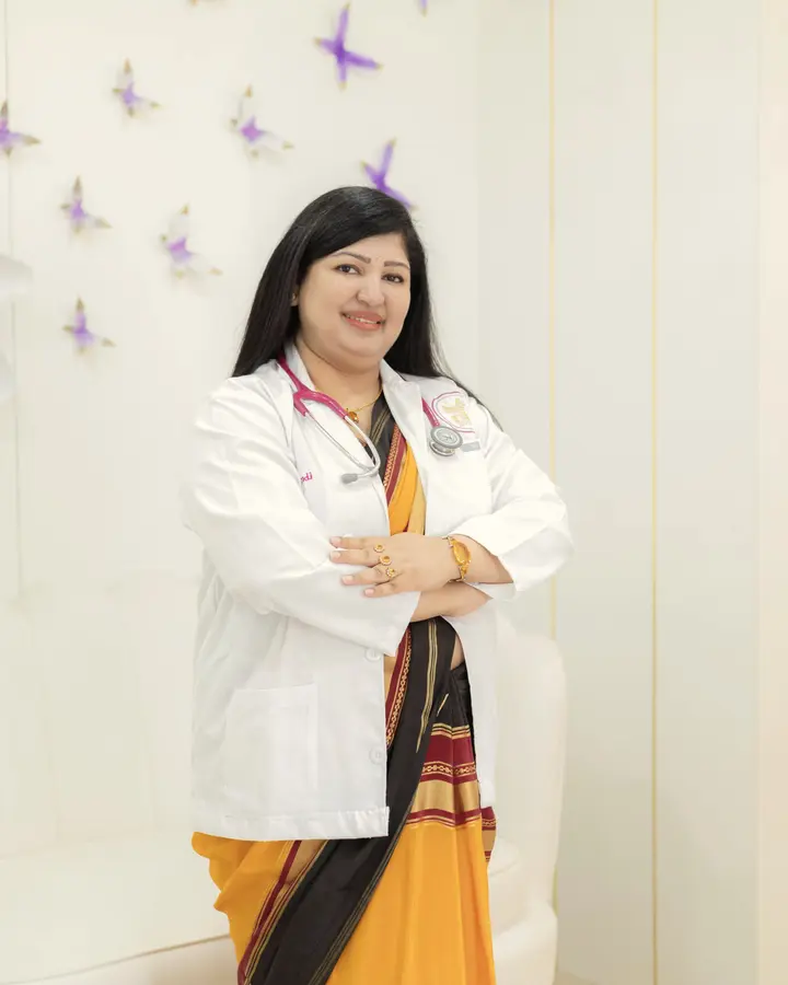 A doctor in a white coat over a sari stands in a bright clinic corridor.