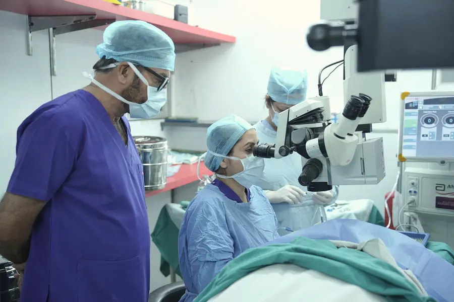 Surgeons in blue scrubs operate under a microscope in a New Delhi hospital theatre.