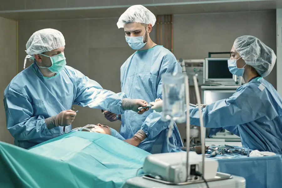 A surgical team in blue gowns and caps operates in a theatre.