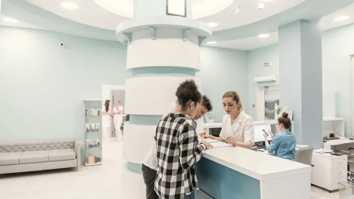 Patients check in at the white front desk of a bright, modern clinic.